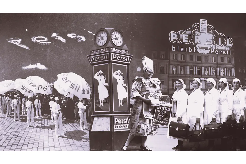 Vintage Persil advertisement collage featuring people holding branded umbrellas, a decorative clock with posters, and a building with illuminated Persil signage in the background.
