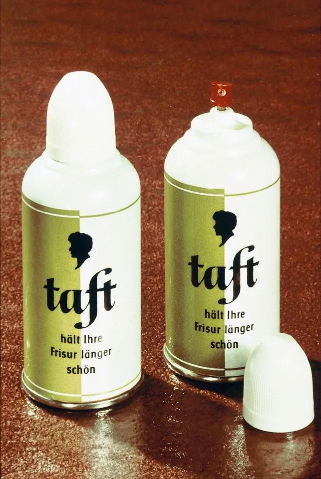 Two vintage Taft hair spray cans with white caps and gold labels placed on a reddish-brown surface