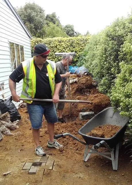 Henkel employees shoveling mulch and loading them into wheelbarrows.